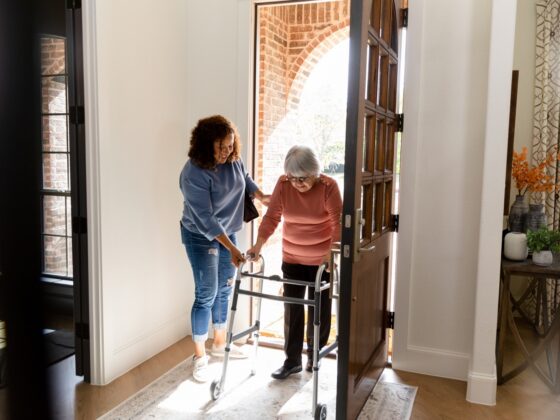 Caregiver helping an older woman with a walker through her front door